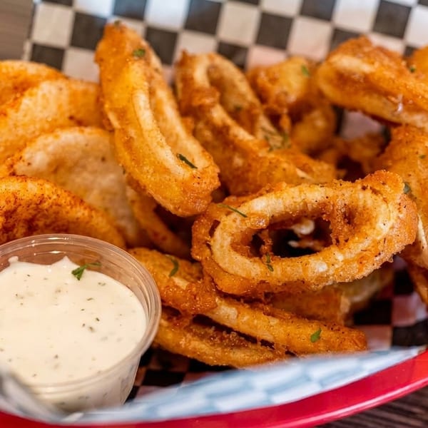 Crispy fried calamari and onion rings with a side of creamy dipping sauce in a red basket.